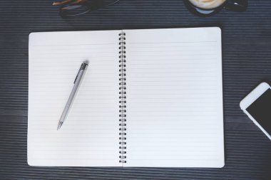 İş kadını elini kalemle kapatıyor. Sayfa defterindeki masa masasını kitap, ekipman gereçleri ve kahve fincanı ile açıyor. Sayfa kağıdında kopyalama alanı olan üst görünüm.