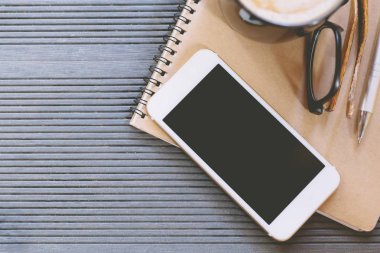 Ofis masasında boş ekranlı beyaz cep telefonu, aksesuar defteri defteri, ekipman malzemeleri. Kopyalama alanı olan üst görünüm. Modern ofis. en üstteki görünüm