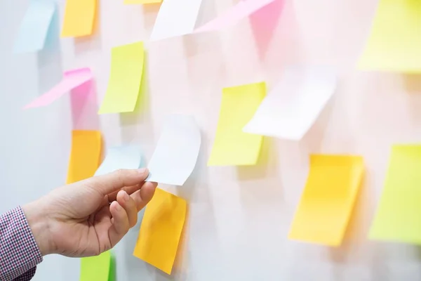 close up people holding paper post it in hand stick wall board. paper note colorful variety reminder sticky notes pin on cork bulletin board background. empty space for text.