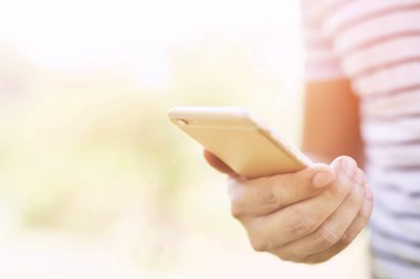 parkta dinlenme sırasında cep telefonu kullanarak genç adam elini yakın. mola sırasında cep telefonu ile mesaj izlerken standı dinlenmek. yumuşak odak.