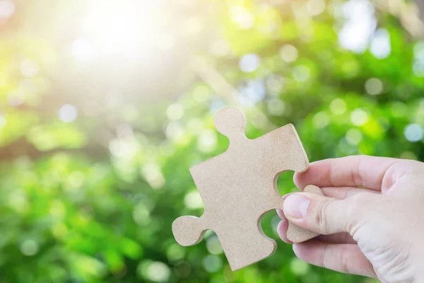 hands person trying to show Jigsaw wooden puzzle piece with tree fresh Morning sunlight background. one part of whole. symbol of association and connection. success and business solution strategy.