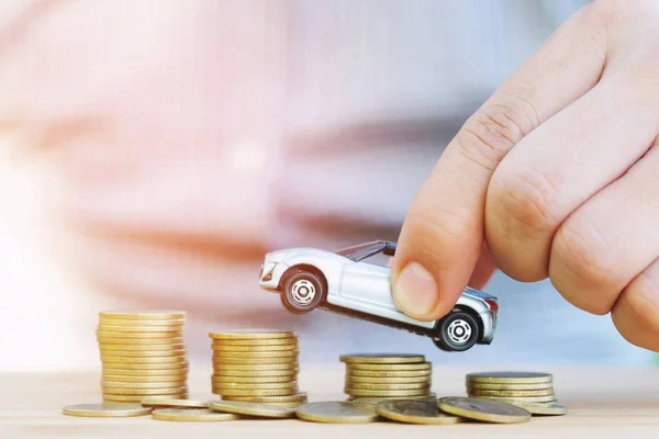 Business man and close up hand holding model of toy car on over a lot money of stacked coins - insurance, loan and buying car finance concept. buy and installments down payment a car.