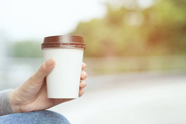 yakın insanlar genç kadın el kamu parkta oturan doğal sabah güneş ışığında kahve içme uzak kağıt fincan tutarak. metin veya logonuz için yer.