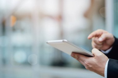 şehre bakan bir ofis binasının önünde dururken bir dijital tablet pc cihazı kullanarak çalışan yakın el İş adamı.