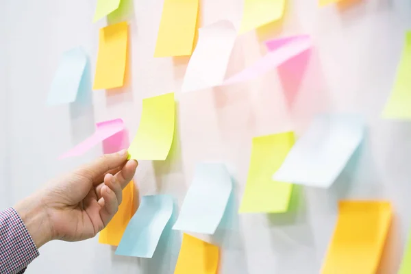 close up hand people business man post it notes in the wall at meeting room. Sticky note paper reminder schedule board. Colorful variety copy empty space. soft focus.
