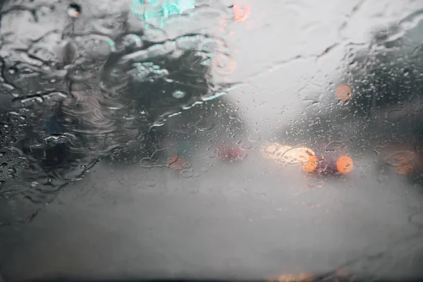 Drops Of Rain Drizzle on the glass windshield in the evening. street in the heavy rain. Bokeh Tail light. soft Focus. Please drive carefully, slippery road. soft focus.