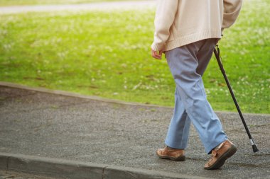 elderly old man with walking stick stand on footpath sidewalk crossing the street alone roadside in public park. concept senior across the street. soft focus clipart