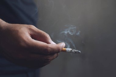 elinde sigara içen adam. Sigara dumanı yayıldı. koyu arka plan