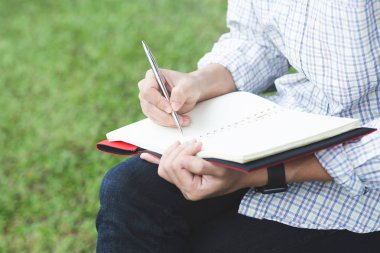 yakın el genç adam kitap içine Kayıt Ders not defteri yazma kalem kullanarak sandalye oturuyor