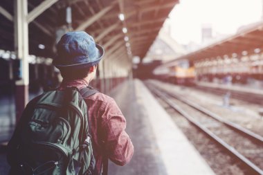 Yolcular Istasyon platformlarını bekliyor. Sırt çantası ile genç Asyalı adam gezgin tren bekliyor. turist seyahat kalkış konsepti için hazır olun.