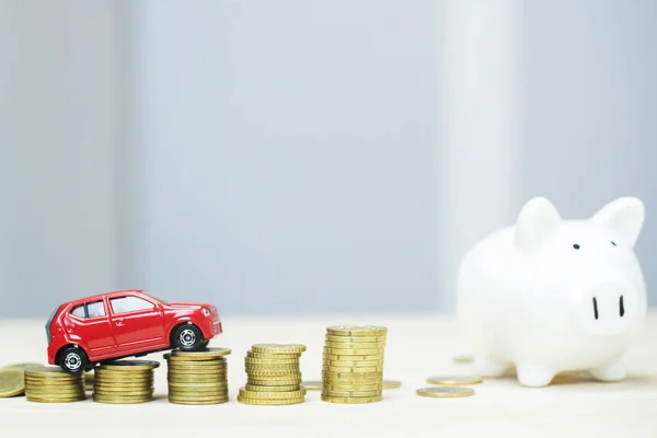 Little red car over a lot of money stacked coins and piggy bank. saving for bank loans costs finance. insurance, buying car finance concept. buy and pay by installments down payment a car. soft focus