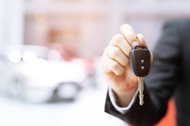Arka planda showroom araba ile araba anahtarı tutan iş adamı el. taşımacılık bayilik ve satış konsepti