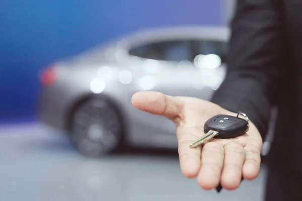 Car key, salesman handing over gives businessman the car key to the other man on car showroom background.