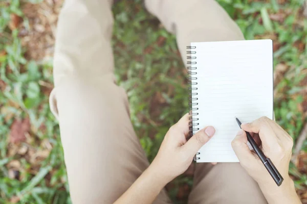 close up hand young man are sitting using pen writing Record Lecture notepad into the book in the parks.