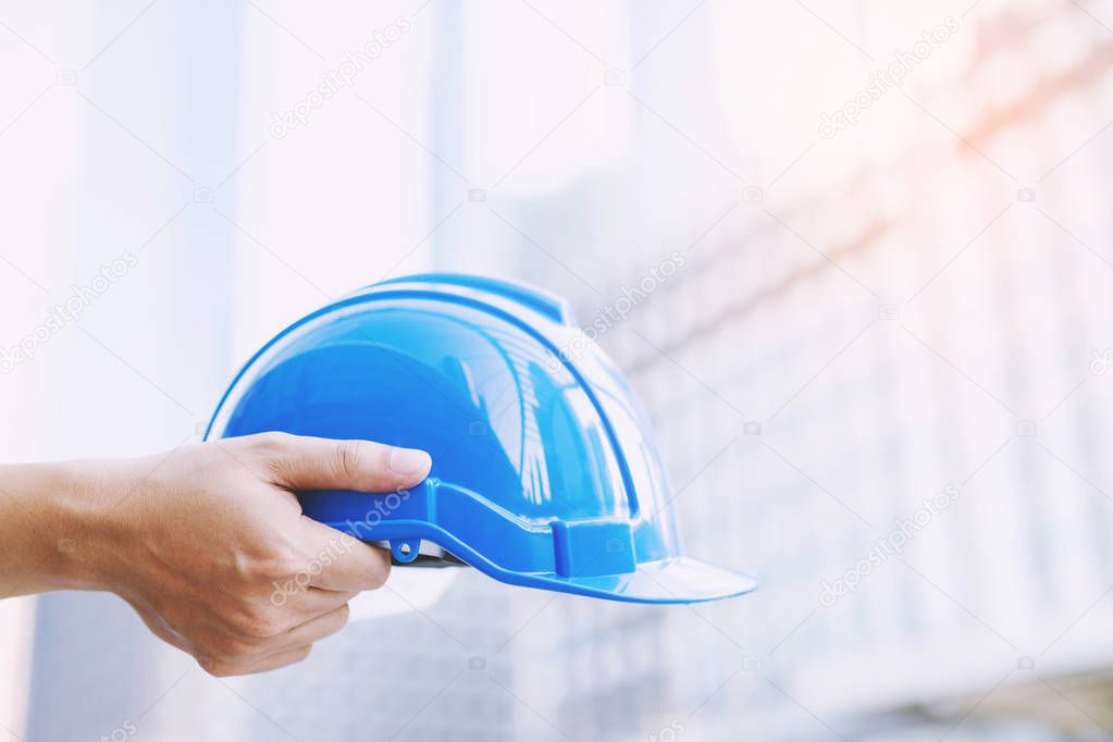 Close up front view of engineering male construction worker stand holding safety white helmet and wear reflective clothing for the safety of the work operation. outdoor of building background.