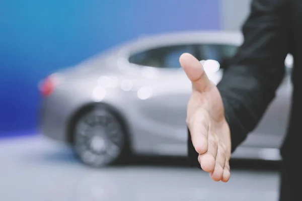 salesman handing over gives businessman the car key to the other man on car showroom background.