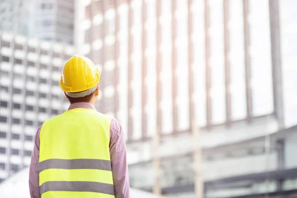 back view of engineering man construction worker wear safety helmet and wear reflective clothing for the safety of the work operation. engineer standing looking project success.