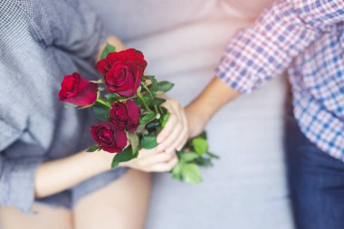 kanepede oturan çift aşıklar genç adam kız arkadaşı mutluluk Love ilk Ilişki tanıttı verilen el sürpriz güzel bir kırmızı gül çiçeği Buket dışarı tutar. Sevgililer Günü Kavramı.