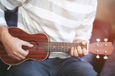 Kanepede akustik gitar ukulele çalan genç adamın ellerinin yakın çekim oturma odası keyfini çıkarın.