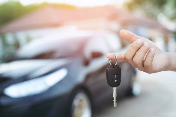 Business man hand holding car keys front with car on background. parking in front of the house. transportation concept