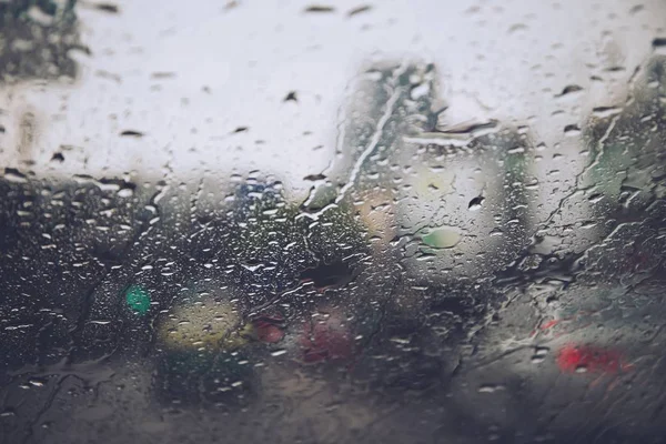 Drops Of Rain Drizzle on the glass windshield in the evening. street in the heavy rain. Bokeh Tail light and Traffic lights. Please drive car carefully, slippery road. soft focus.