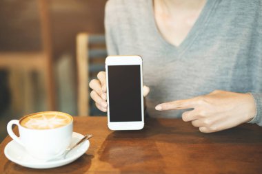 kafede kahve içerken boş masaüstü ekranı ve parmak dokunmaile cep akıllı telefon tutan kadın el.