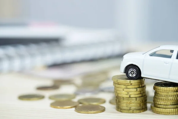 Little white car over a lot of money stacked coins and background accounting document calculate installment. for bank loans costs. insurance, car finance concept. buy and pay by down payment a car.