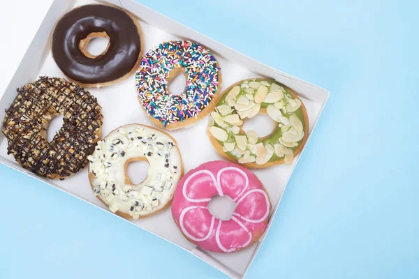 assorted donuts with chocolate frosting, topping sprinkles donuts Colorful variety and Variety of flavors mix of multi colored sweet donuts with frosted sprinkled in box on blue background. top view