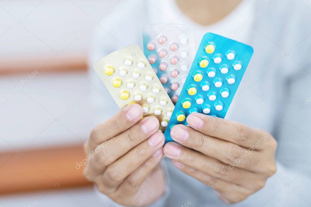 Close up young women hand holding contraceptive pill on with colorful pills strips. Contraception reduces childbirth and pregnant concept.