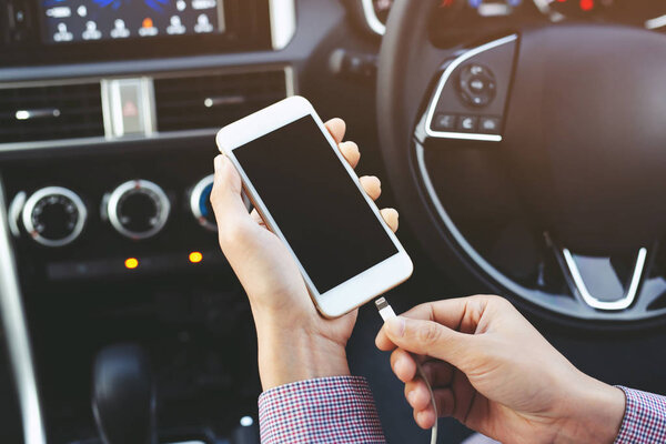 Закрыть человек руку держа заряд батареи мобильного смартфона в машине. Оставьте свободное место на экране
.