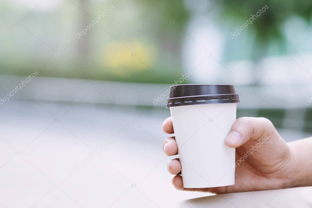 close up people young female hand holding paper cup of take away drinking coffee on natural morning sunlight. space Place for your text or logo.