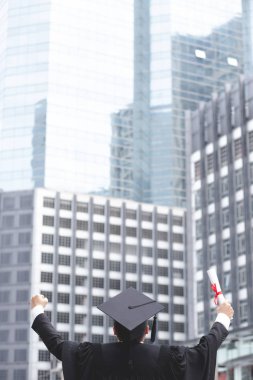 Mutlu mezunlar genç adam elinde Sertifika kağıt tutarak ayakta kollar yumruk neşeli göstermek başarı arka plan bina Konsept eğitim tebrik diploması Üniversite mezunu