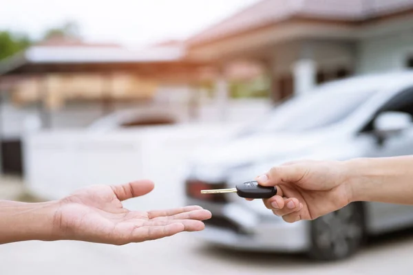 Business man hand holding car keys front with new car on background. parking in front of the house. transportation concept. Leave copy space to write messages text.