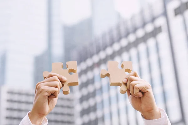 two hand business man show trying to connect Jigsaw wooden puzzle piece with office building background. one part of whole. symbol of association and connection. success and business solution strategy