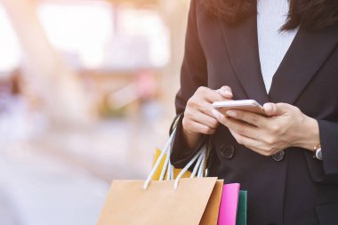 Moda mağazasında alışveriş yapmak için bir sürü alışveriş çantası tutan bir iş kadını. Müşteriler internet üzerinden alışveriş yapmak için cep telefonu kullanabilirler. Satın alma ve ödeme havalesi için..