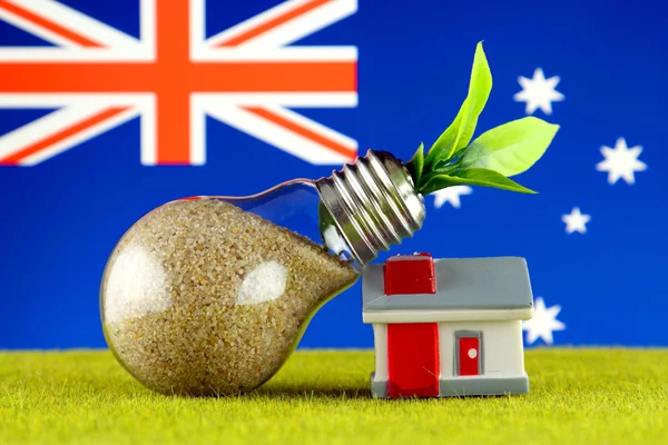Plant growing inside the light bulb, miniature house on the grass and Australia Flag. Renewable energy. Electricity prices, energy saving in the household.