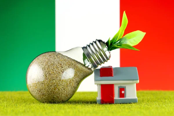 Plant growing inside the light bulb, miniature house on the grass and Italy Flag. Renewable energy. Electricity prices, energy saving in the household.