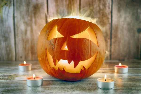Halloween pumpkin with smoke and candles on wooden background.