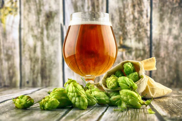 Glass of craft beer and fresh hop cones on a wooden background.