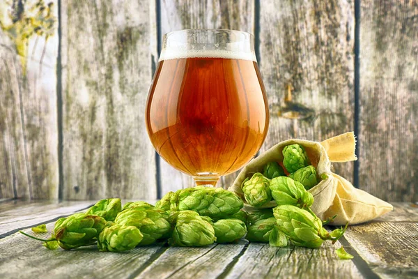 Glass of craft beer and fresh hop cones on a wooden background.