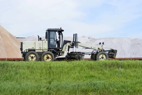 The grader is at the dam with pipeline in the background of mine. Side view. Foreground green grass — Stock Photo, Image