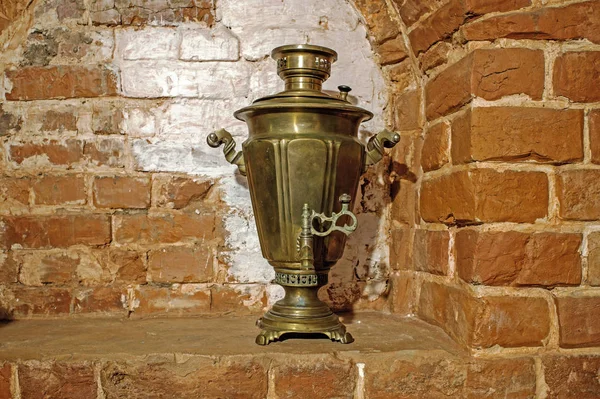 Ancient copper samovar stands in the form of scenery on the background of the fireplace wall of red brick. Background, retro, vintage.