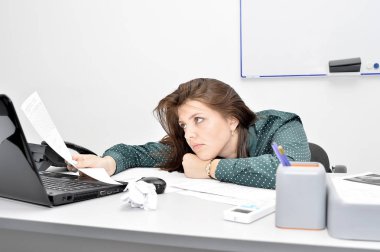 Yorgun bir poz içinde belgili tanımlık laptop ofiste kahverengi saçlı kız, düşünceli belge içinde görünüyor..