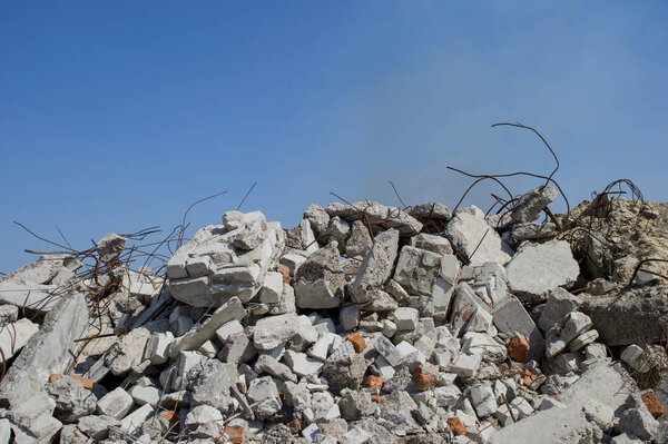 Арматура, торчащая из груды кирпичных щебня. На заднем плане видны остатки дымовых клубов
