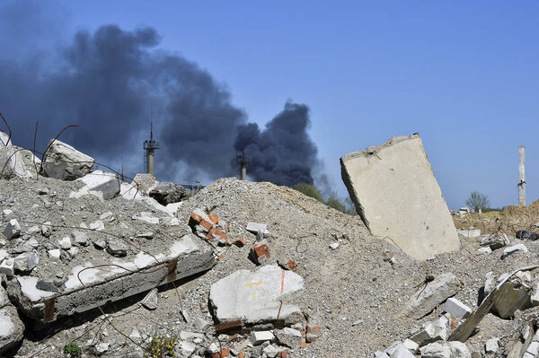 Concrete slab stuck in the ground against the background of a Smoking electrical substation. A symbol of the devastation of war. Background, place of inscription.