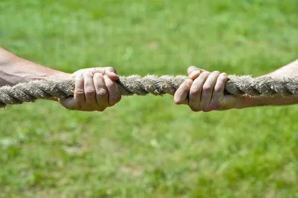 Two men\'s hands pull the rope each in his own direction. The concept of dispute, conflict and force.