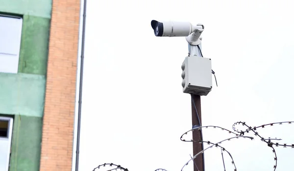 Videovigilancia de la cámara en el fondo del edificio montado en una pared de ladrillo, vallado con alambre de púas —  Fotos de Stock