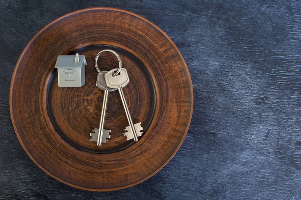 A bunch of keys lie on a vintage plate, along with an imitation of the house in the form of a metal layout. The concept of the offer of sale of real estate. Copy space.