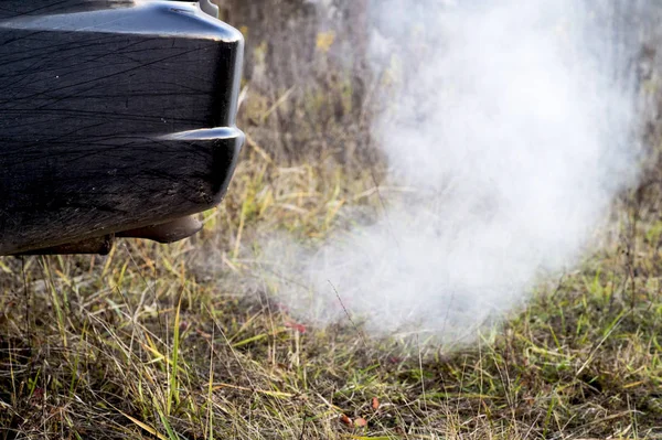 The back of the black car with the emission of smoke from the exhaust pipe on the background of nature. The concept of environmental pollution by vehicles.