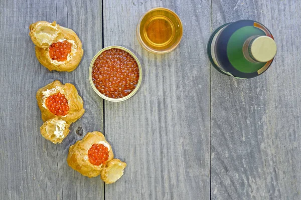 Eklerleri kırmızı havyar, bir kutu, bir şişe ve bir bardak konyak ahşap rustik antika arka plan üzerinde havyar ile.